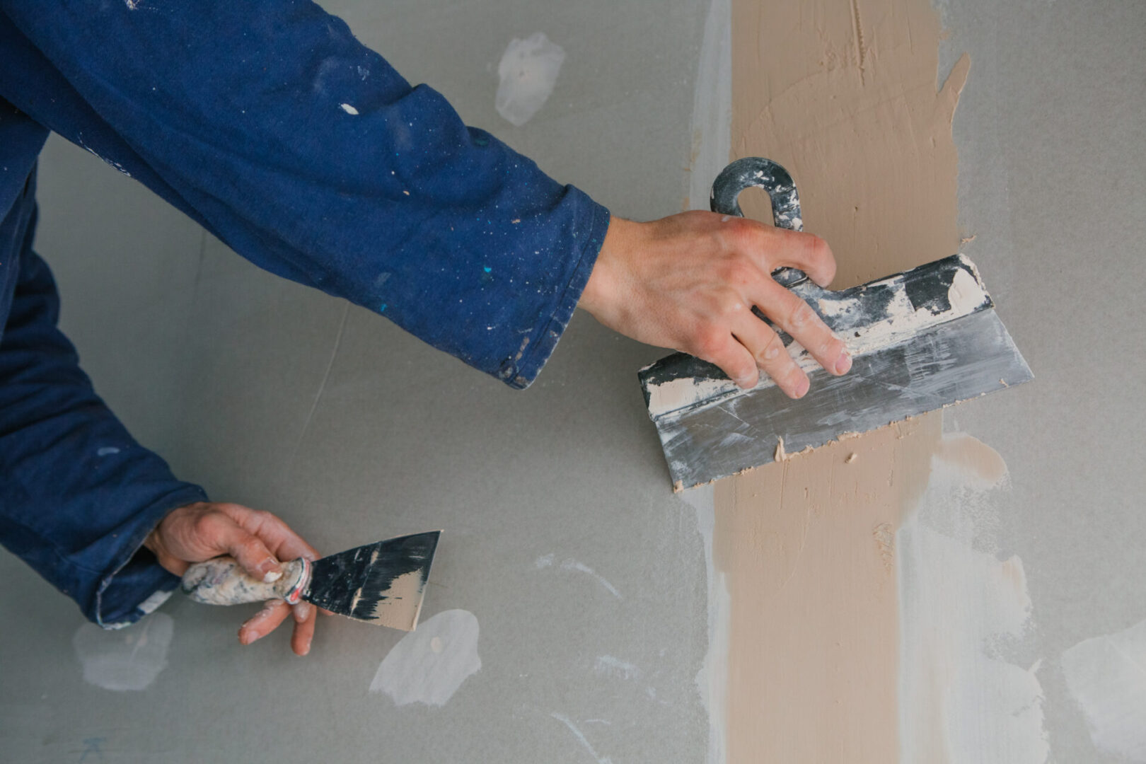 A person is using a spatula to spread paint on the wall.